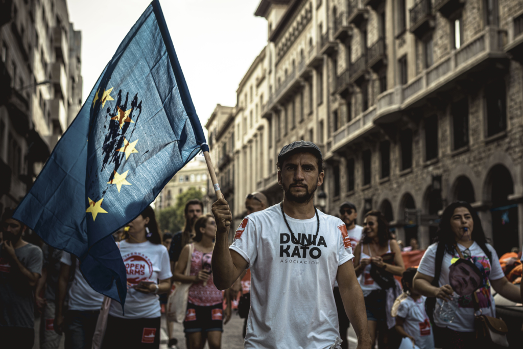July 13, 2019 - Barcelona, Catalonia, Spain - A human rights activist with a bloodstained EU flag protests over the plight of migrants crossing the Mediterranean