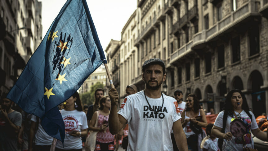 13 de julio de 2019 – Barcelona, Cataluña (España) – Un activista de los derechos humanos con una bandera de la UE ensangrentada se manifiesta en protesta por el sufrimiento de los inmigrantes que cruzan el Mediterráneo