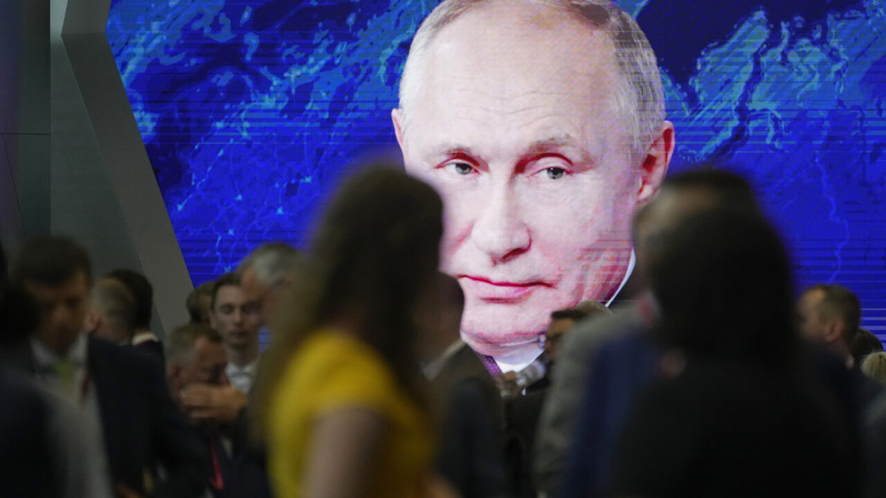 Participants walk past a screen showing Russian President Vladimir Putin at the St. Petersburg International Economic Forum in St.Petersburg, Russia