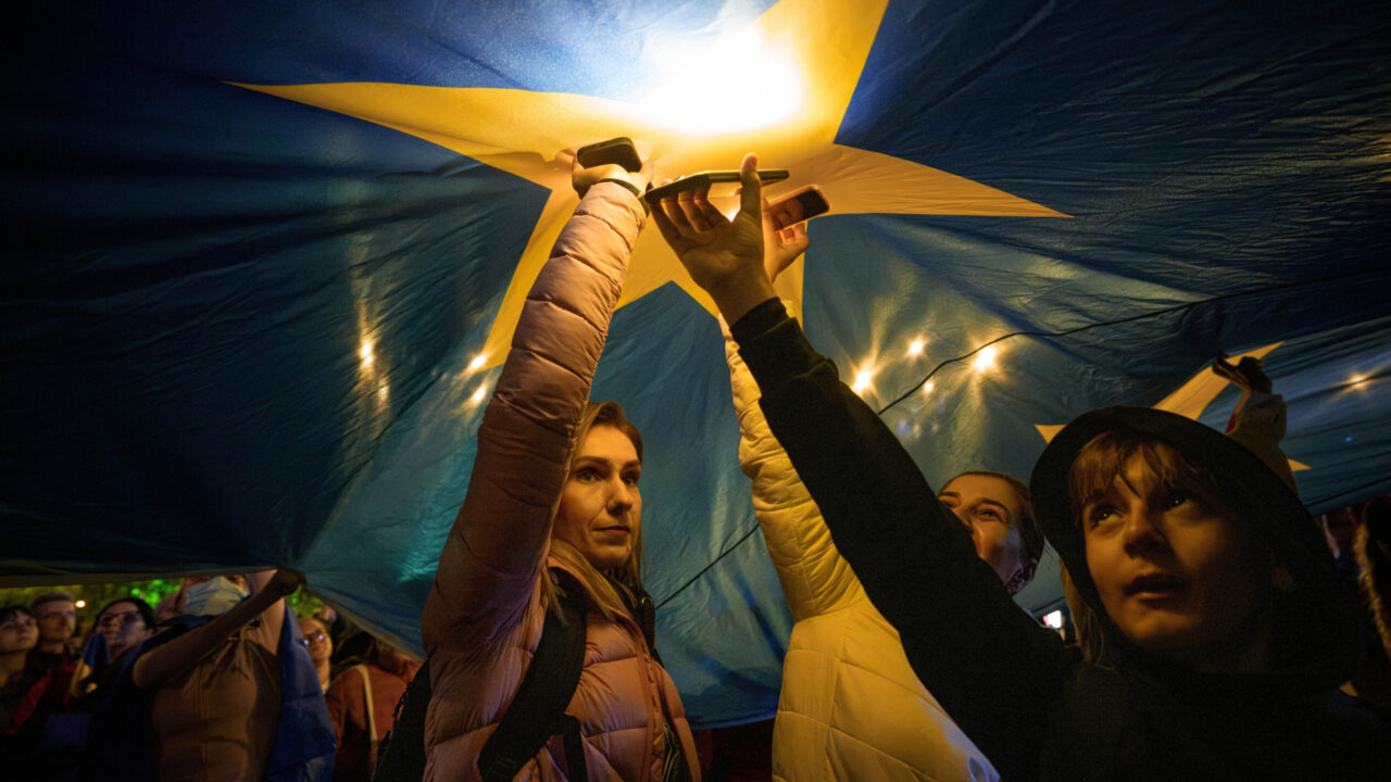 Demonstrators shine the lights of their mobile phones as they stand under a large European Union flag, during a pro-EU rally ahead of the second round of the presidential election redo in Bucharest, Romania, Friday, May 9, 2025. (AP Photo/Andreea Alexandru)