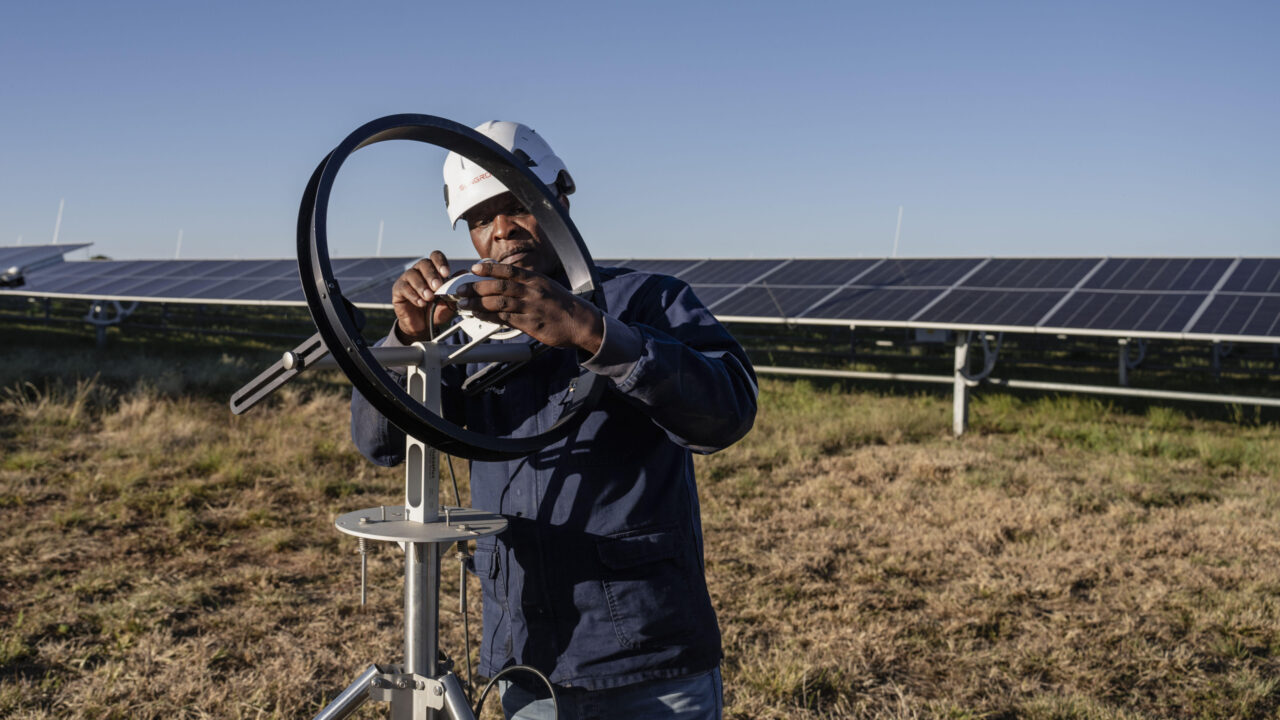 A man in a hard hat sets up a piece of machinery in front of a solar power plant in South Africa