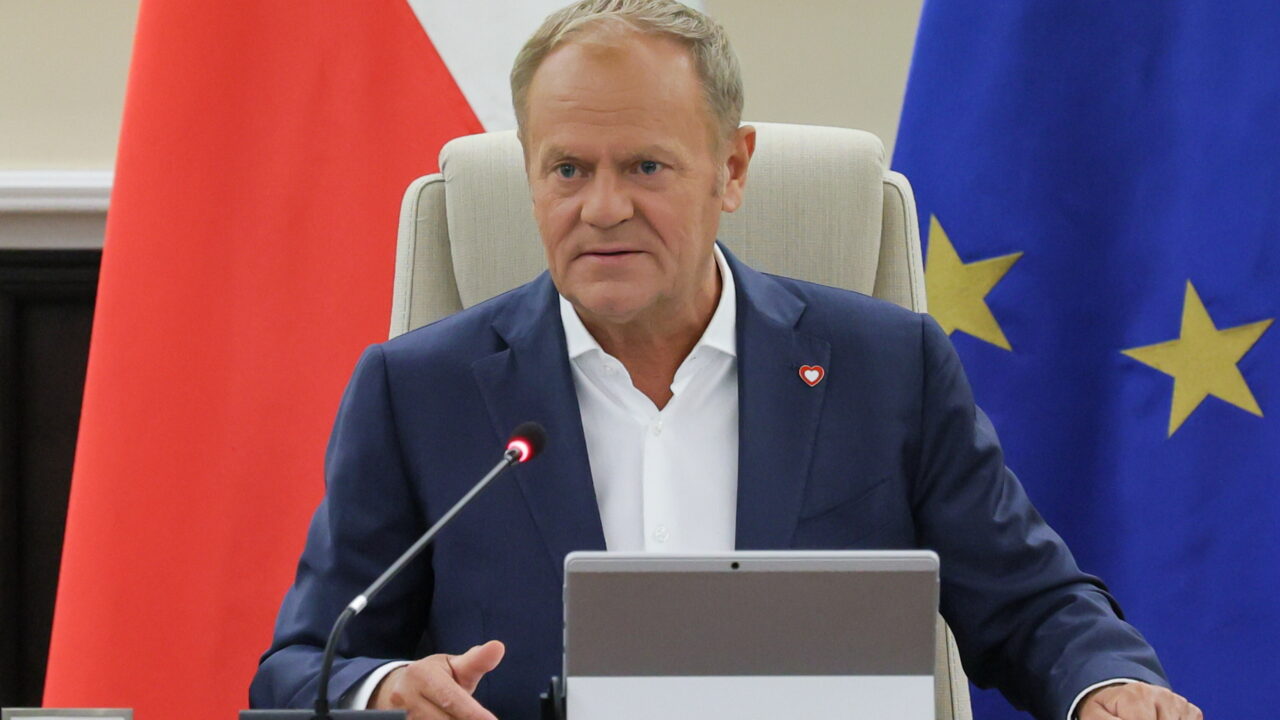 Polish Prime Minister Donald Tusk pictured at a desk, in front of the flags of Poland (left) and the EU (right)