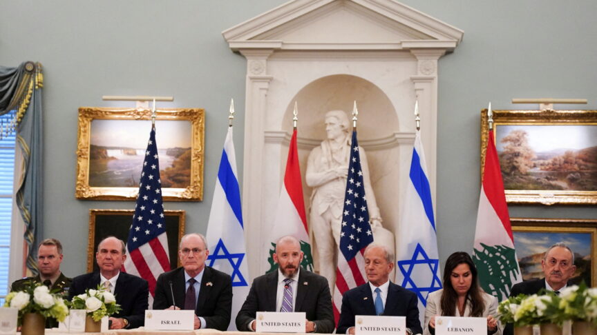 Ein Foto zeigt eine Gruppe von Delegierten an einem Tisch bei einer offiziellen Besprechung in einem Saal mit Fahnen, Blumen.