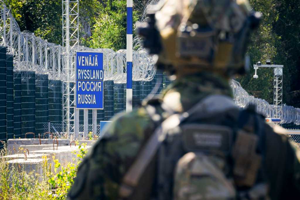 Ein Foto zeigt einen Soldaten in Tarnuniform, von hinten stehend vor einem Grenzschild und Stacheldrahtzaun am Übergang.