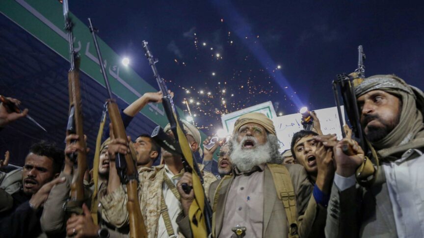 Ein Foto zeigt eine Menschenmenge mit erhobenen Gewehren und Schildern, die nachts auf einer Straße in Sanaa Lichter hochhalten.