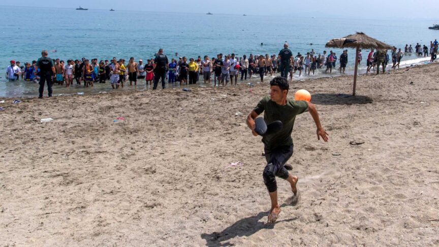 Ein Foto zeigt einen Mann am Strand, der barfuß wegläuft und einen Ball trägt, während Menschen aus dem Meer kommen.
