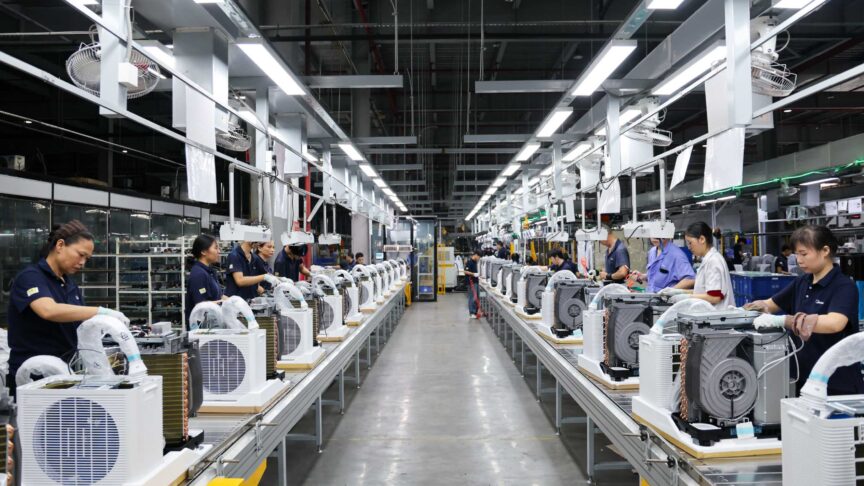 Ein Foto zeigt Arbeiter an einer Produktionslinie, die portable Split-Klimageräte in einer großen Fabrikhalle montieren.