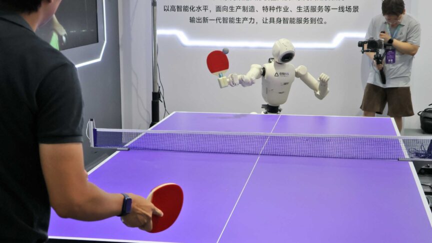 Ein Foto zeigt einen humanoiden Roboter beim Tischtennis gegen eine Person an einem lila Tisch.