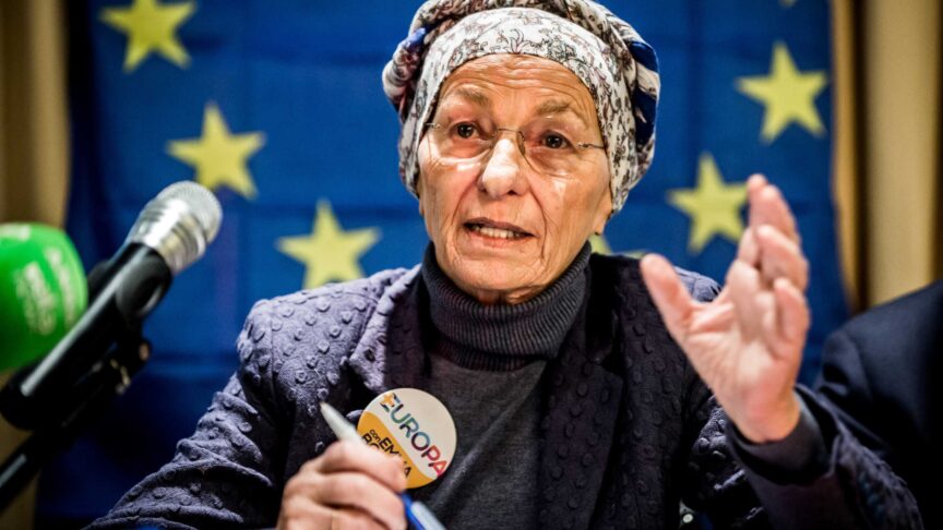 Ein Foto zeigt eine ältere Frau mit Kopftuch, die spricht, bei einer Pressekonferenz vor einer EU-Flagge.