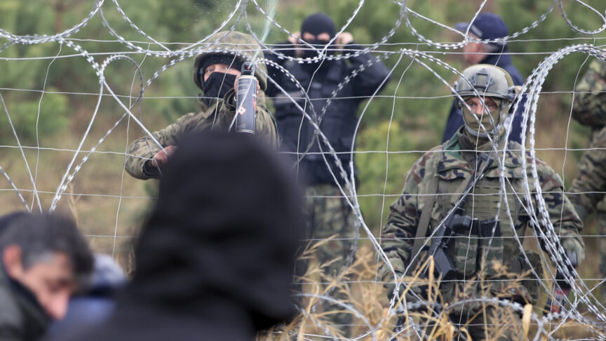 Polish border guards stand near the barbed wire as migrants from the Middle East and elsewhere gather at the Belarus-Poland border near Grodno, Belarus, Monday, Nov. 8, 2021. Poland increased security at its border with Belarus, on the European Union’s eastern border, after a large group of migrants in Belarus appeared to be congregating at a crossing point, officials said Monday. The development appeared to signal an escalation of a crisis that has being going on for months in which the autocratic regime of Belarus has encouraged migrants from the Middle East and elsewhere to illegally enter the European Union, at first through Lithuania and Latvia and now primarily through Poland. (Leonid Shcheglov/BelTA via AP)