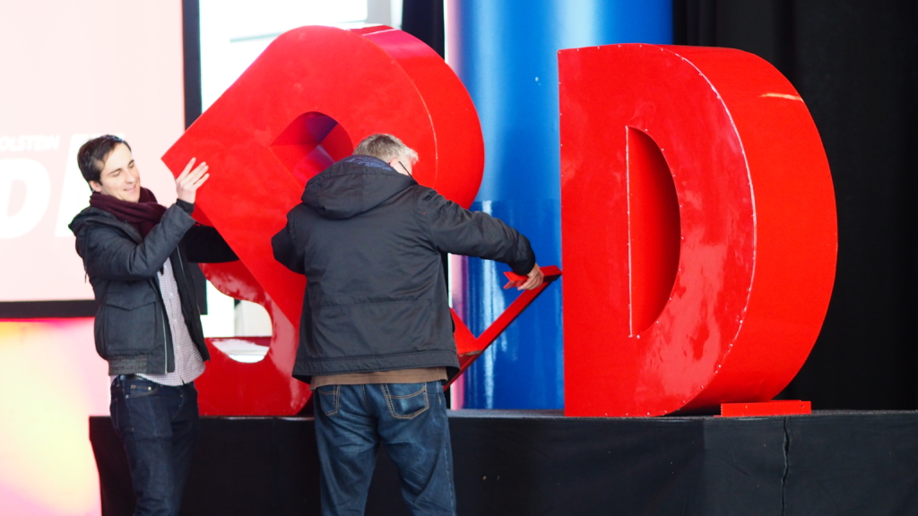 Two men take apart a giant SPD sign at a party conference