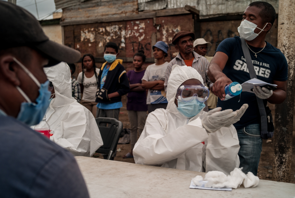 A medical worker in Madagascar in full PPE sanitises their hands while testing people for covid/19