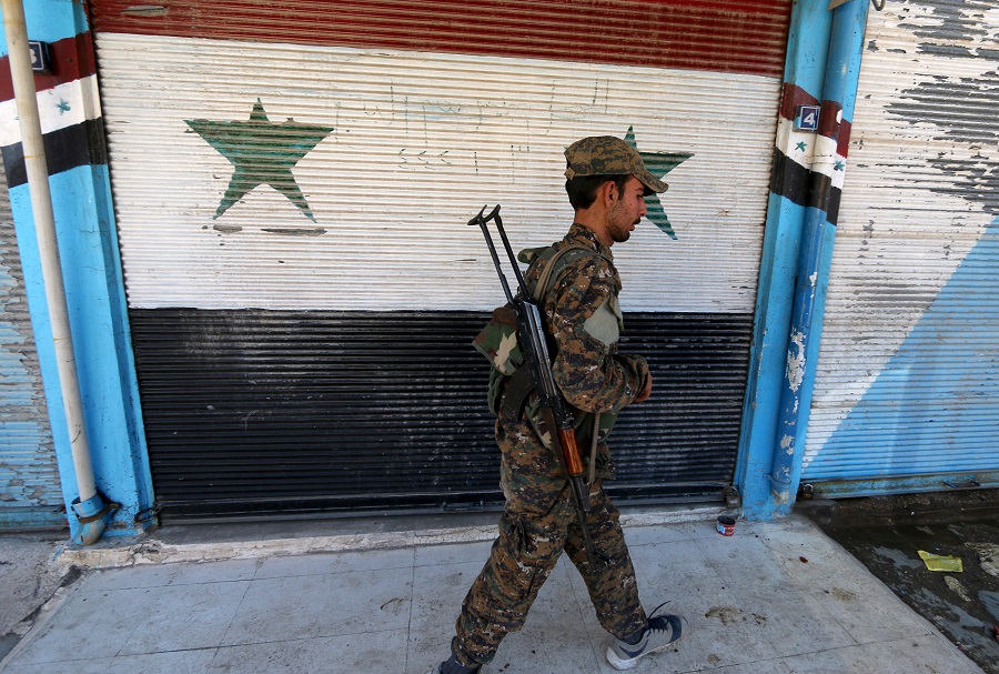 A Kurdish fighter from the People's Protection Units (YPG) walks past a shop with Syrian national flags painted on its shutter in the southeast of Qamishli city, Syria, April 22, 2016. REUTERS/Rodi Said